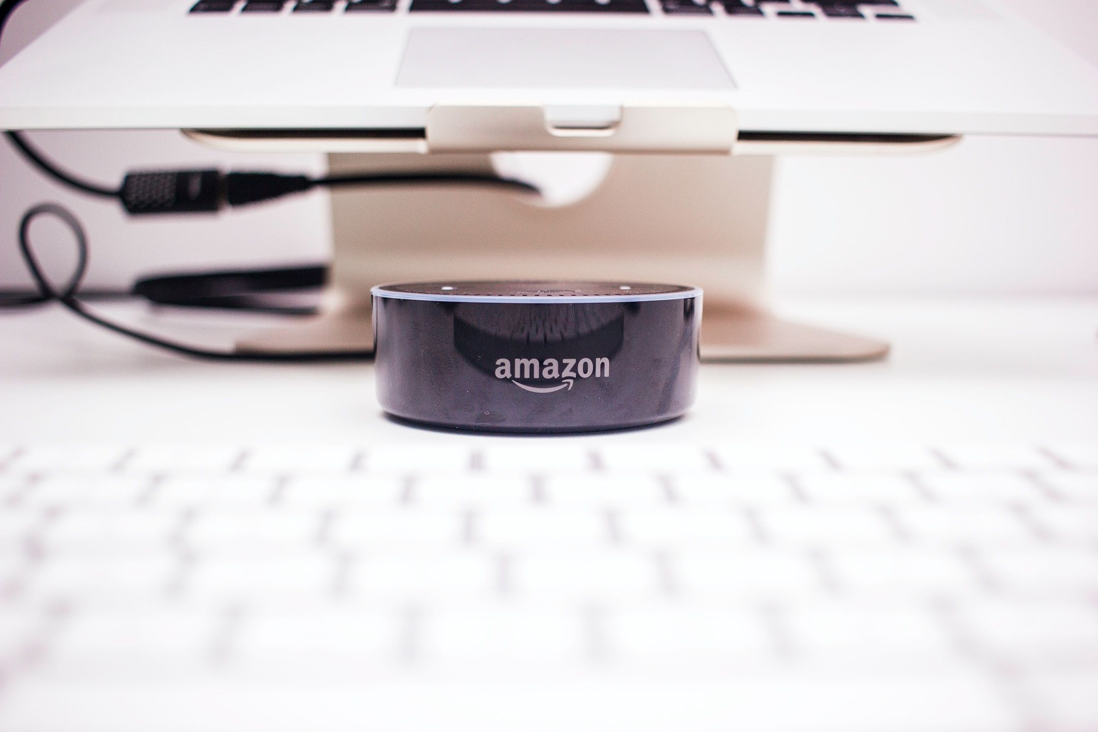 Un Amazon Echo Dot noir sous un Macbook et au-dessus d'un clavier Apple.